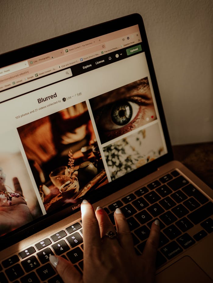 Hand browsing stock images on laptop with warm sunlight casting shadows indoors.
