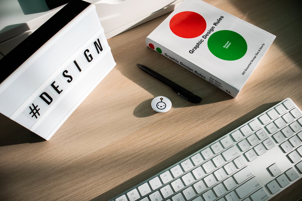 Bright desk setup featuring design book, keyboard, and hashtag lightbox for creativity.